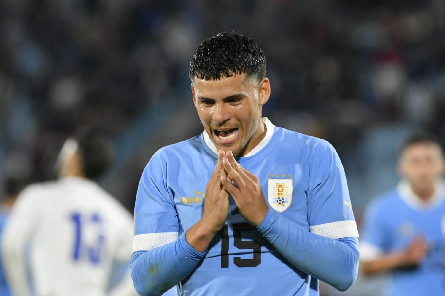  Maximiliano Araujo, a Uruguayan soccer player, wearing the national team's blue jersey with the number 19, celebrates a goal with his hands together in front of his mouth.